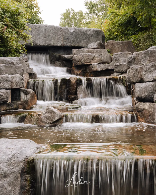 Une petite cascade en gradins coule entre des blocs de pierre et la verdure.