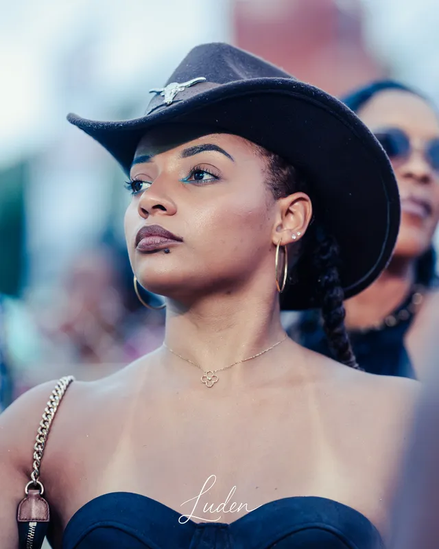 Une femme au chapeau noir de cow-boy regarde au loin, au milieu de la foule.