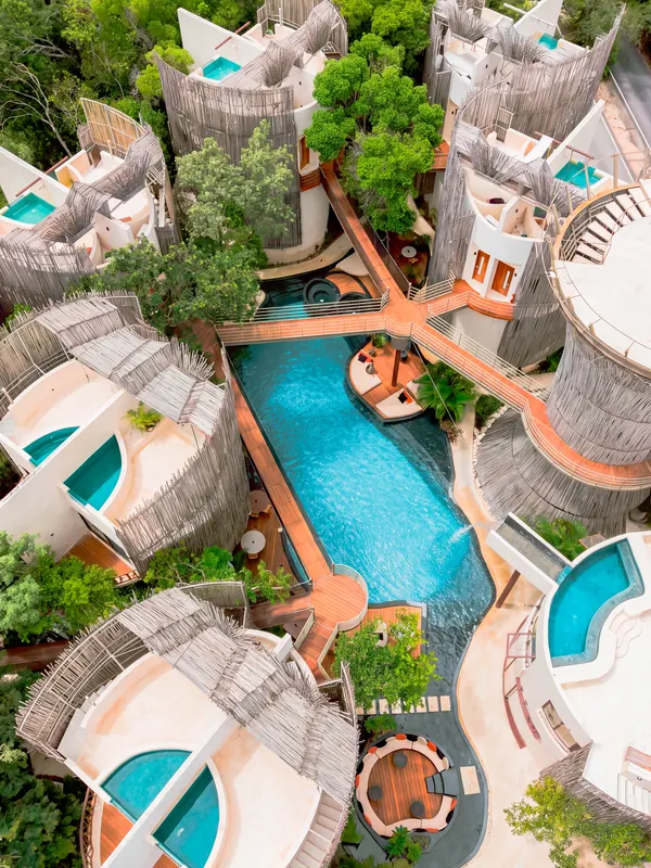 Un hôtel vu du ciel : piscine turquoise, passerelles et végétation.