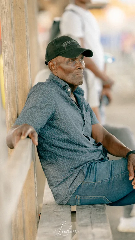 Un homme âgé à casquette sombre, assis sur un banc en bois.