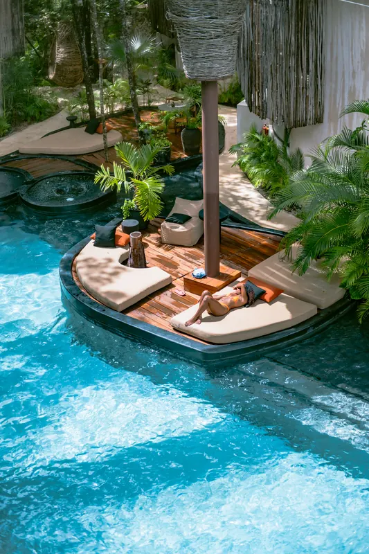 Une piscine turquoise avec un îlot de transats, vue d’en haut.