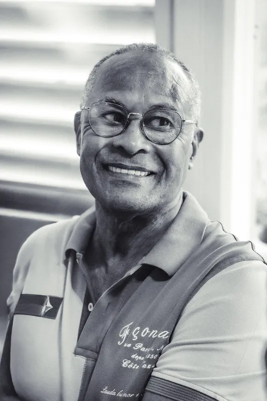 Portrait en noir et blanc d’un homme souriant, lunettes sur le nez, en polo à col.