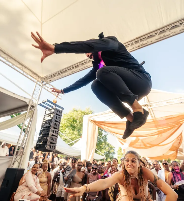 Un danseur en plein saut sous un chapiteau blanc, devant la foule.